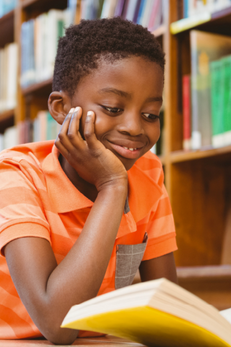 young boy reading a book in the library and smiling