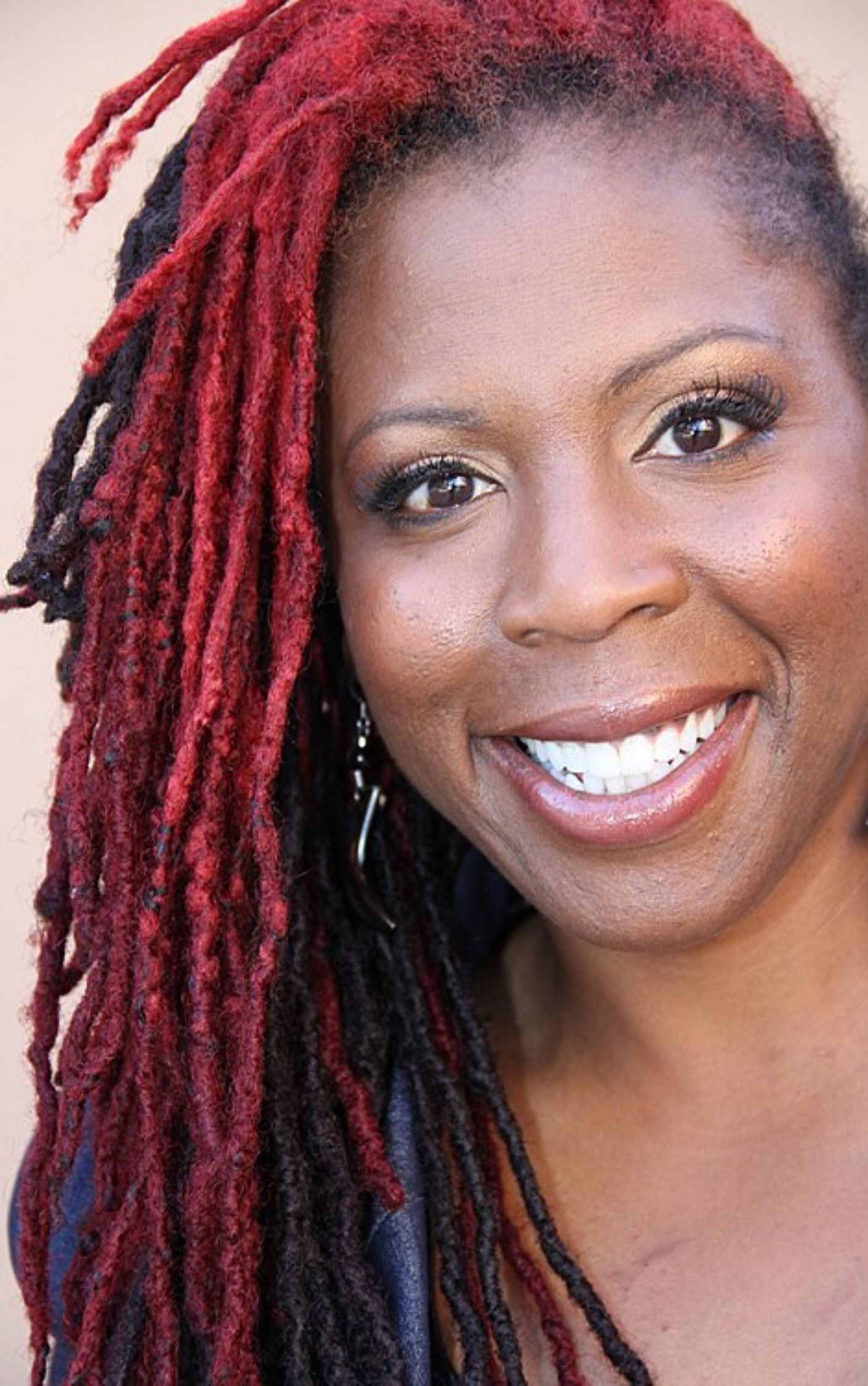 Jasmyne Cannick smiling with red and black locs; journalist and advocate for Black LGBTQ+ workers' rights.